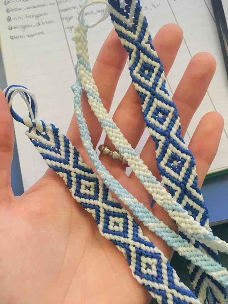 two blue and white braided bracelets being held by someone's hand