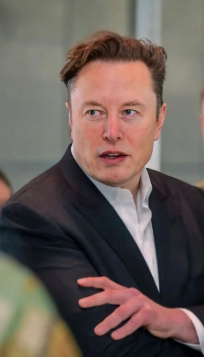 a man in a suit and tie with his arms crossed looking at the camera while standing next to other people