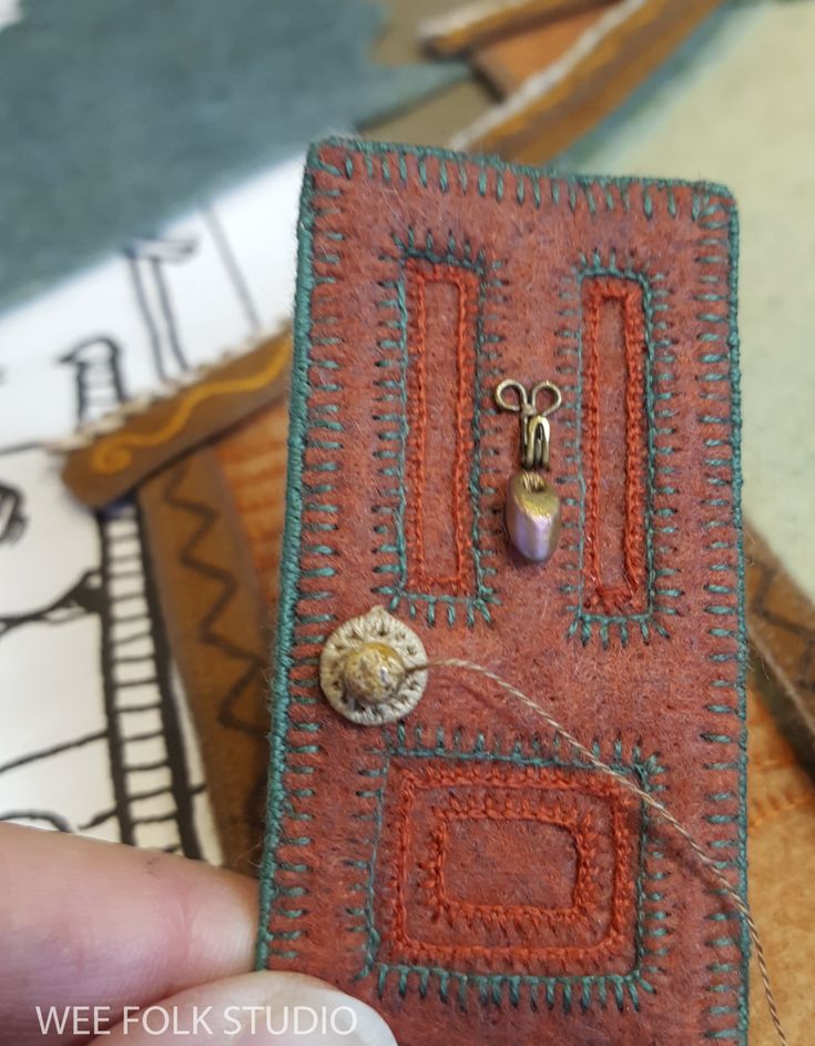 a hand holding a small piece of fabric with buttons and beads on it, in front of other items