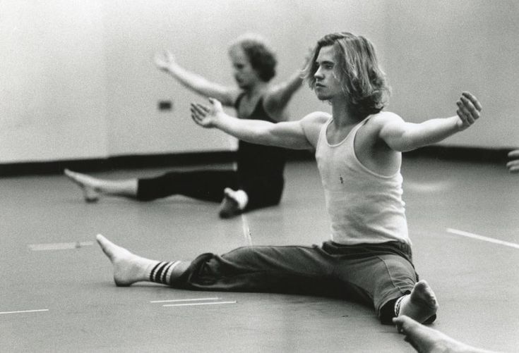 two people sitting on the floor with their arms spread out and one person standing up