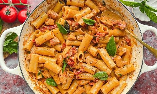 a pan filled with pasta and sauce on top of a table next to tomatoes, basil leaves and other vegetables