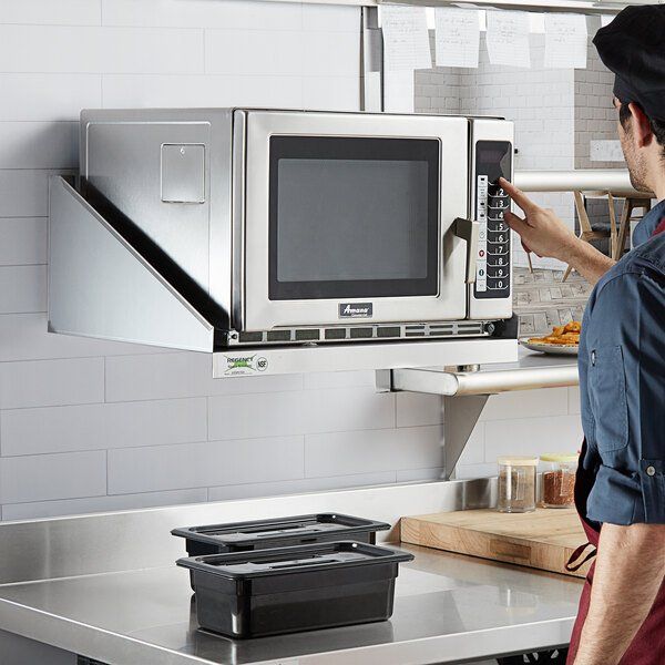 a man is pointing at a microwave on the wall in a kitchen with stainless steel counter tops