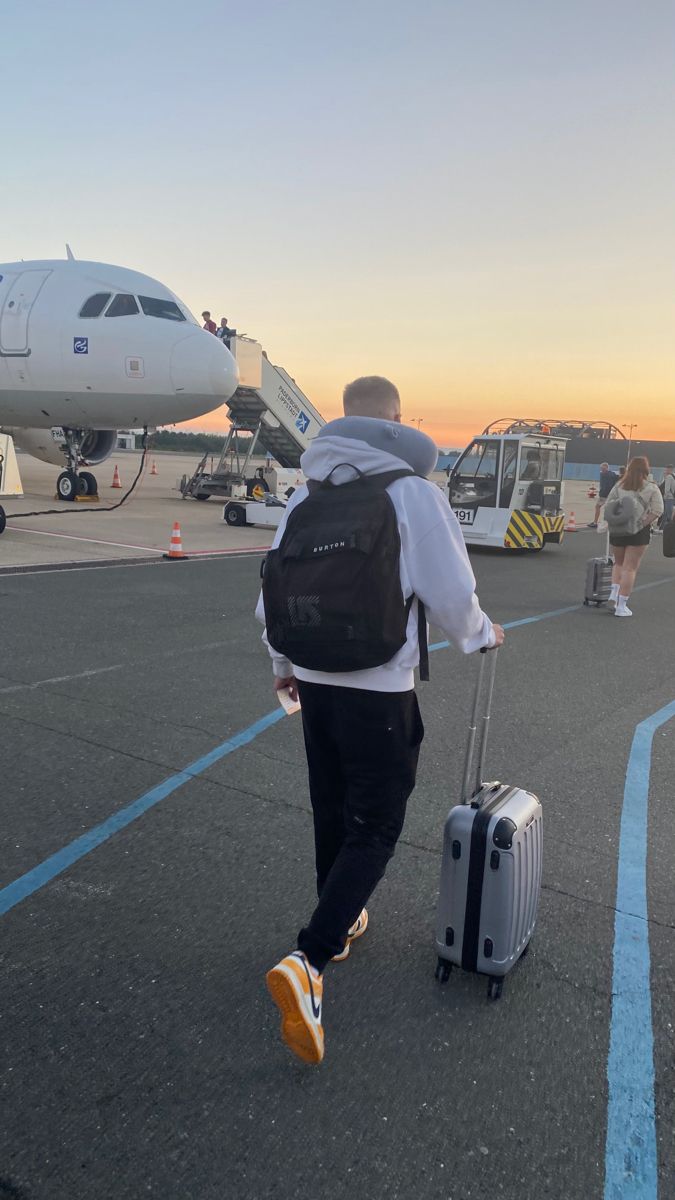 a man with a backpack and suitcase walking towards an airplane