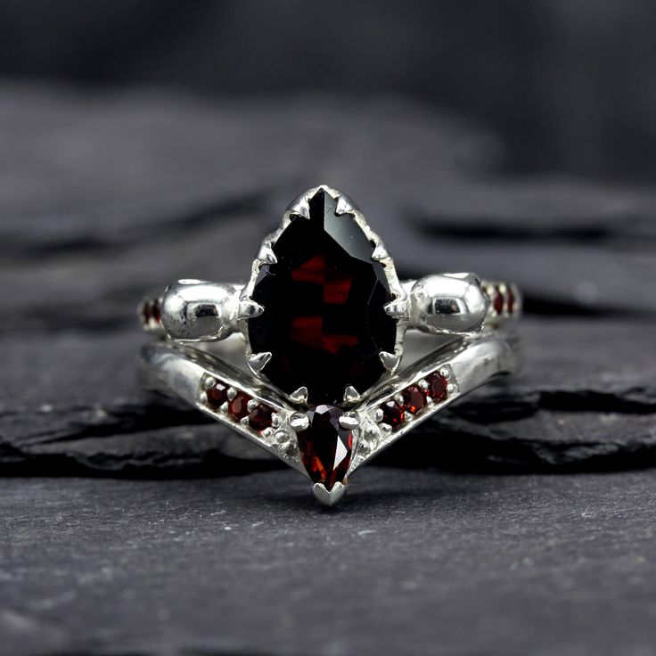 Add a touch of sparkle to your special day with our Garnet Wishbone Wedding Ring. This silver ring features a stunning garnet gemstone and a gothic wishbone design, symbolizing your everlasting love. Let this ring be a beautiful reminder of your commitment. If you require the wedding ring service please select "stock size" for terms click here Hallmarked by Birmingham Jewellery Quarters Assay Office as your guarantee of quality. ⸸ Metal: Sterling Silver⸸ Gemstones: Garnet⸸ Band Width: 3.5 mm⸸ We Detailed Wedding Bands For Women, Gothic Diamond Ring, Goth Engagement Rings Silver, Dark Red Wedding Ring, Gothic Promise Ring, Wedding Ring Garnet, Red Engagement Ring Silver, Wedding Ring Gothic, Wedding Ring Goth