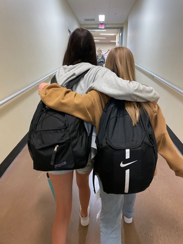 two girls with backpacks walking down a hallway