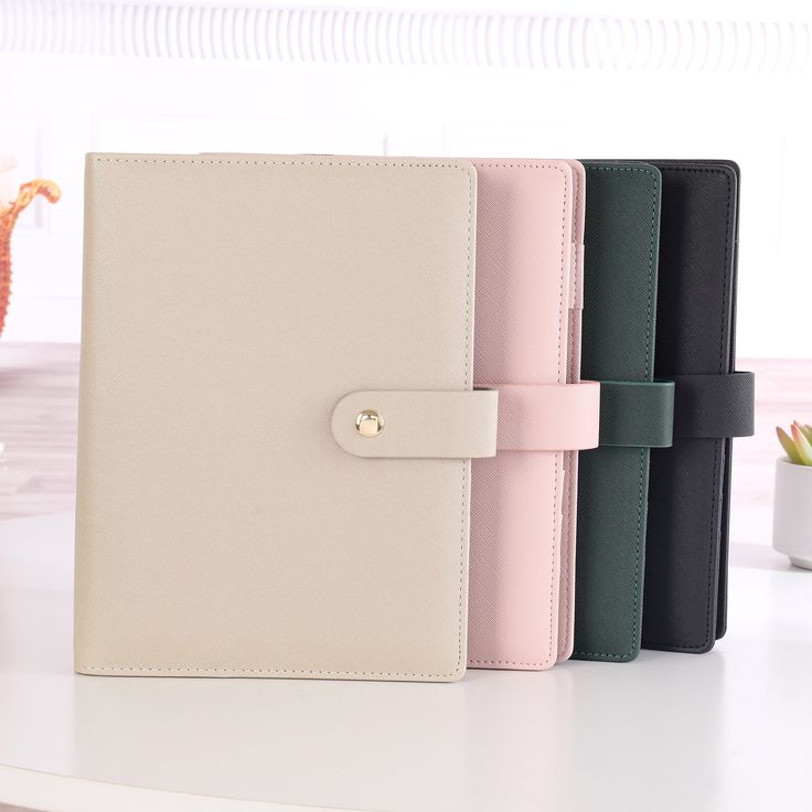 four different colored notebooks sitting next to each other on a white table with a plant in the background