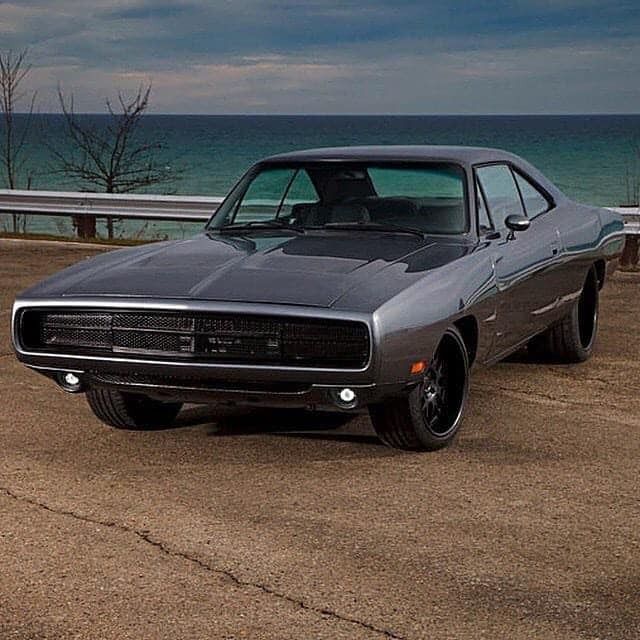 a gray muscle car parked in front of the ocean