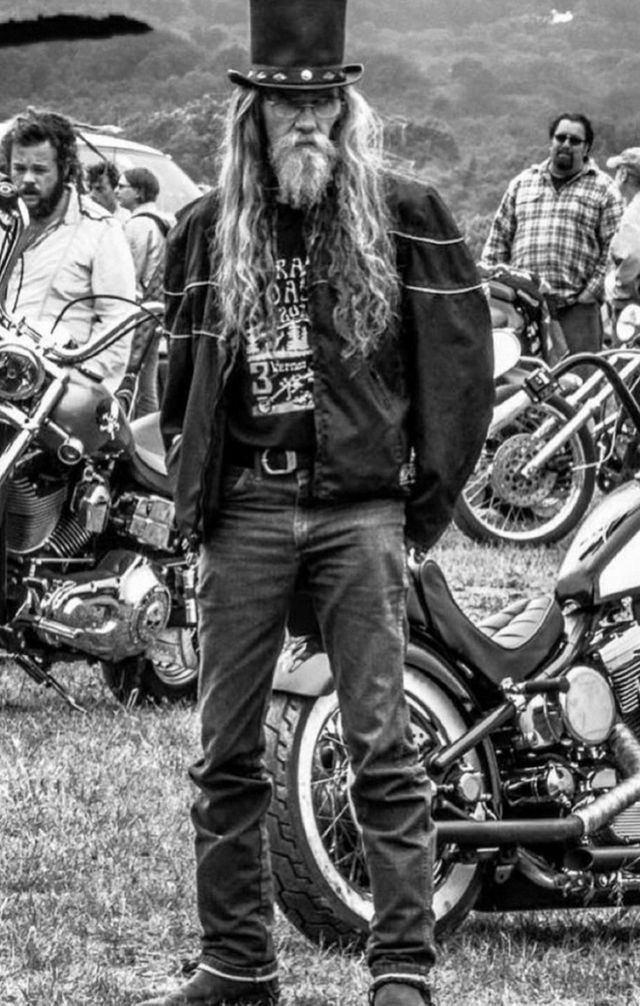 a man with long hair wearing a top hat standing next to motorcycles