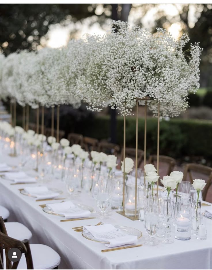 a long table with white flowers in vases and place settings on the tables is set for an event