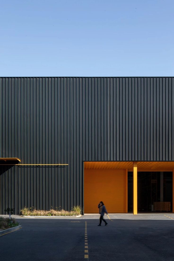 a person walking down the street in front of a black building with yellow doors and windows