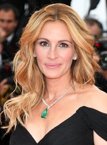 a woman with long blonde hair wearing a green necklace and black dress smiling at the camera