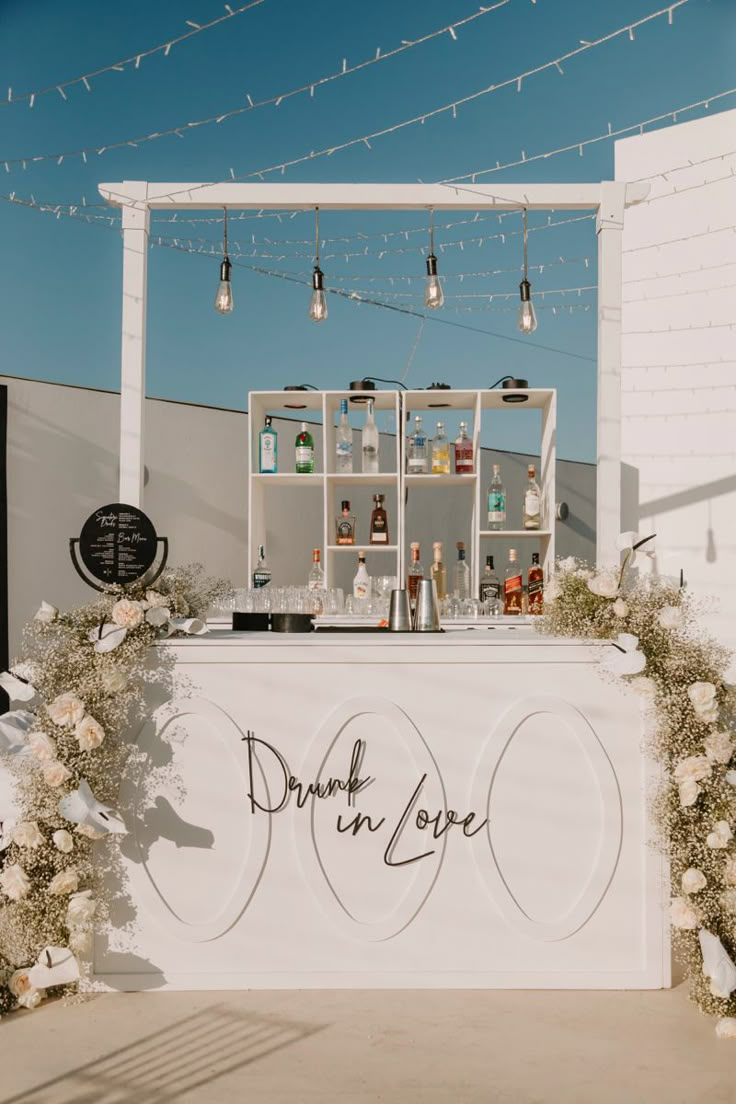 an outdoor bar set up with flowers and bottles on the counter for drinks to be served