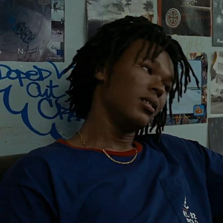 a young man with dreadlocks sitting in front of a wall covered in posters