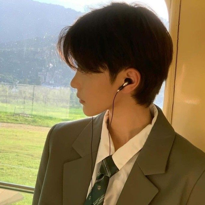 a young man wearing ear buds looking out the window at grass and mountains in the distance