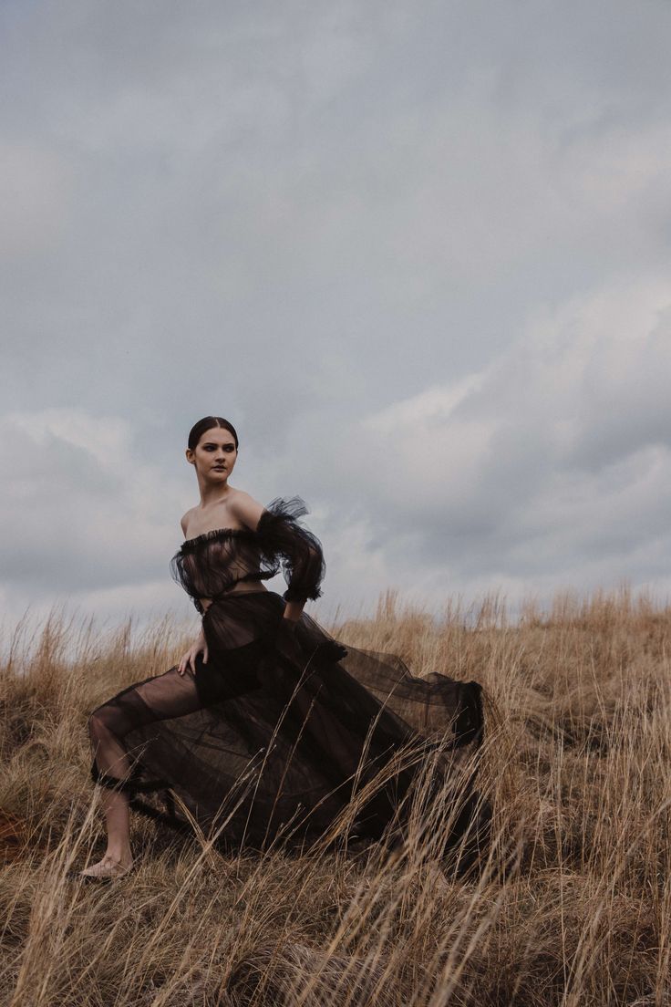 a woman in a black dress sitting on top of a dry grass field