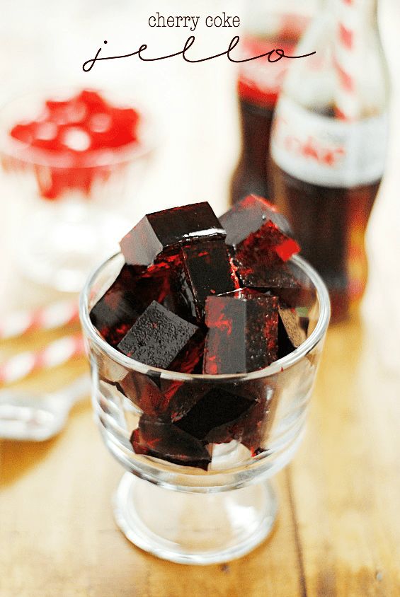 a glass bowl filled with red and black jello next to a bottle of coke