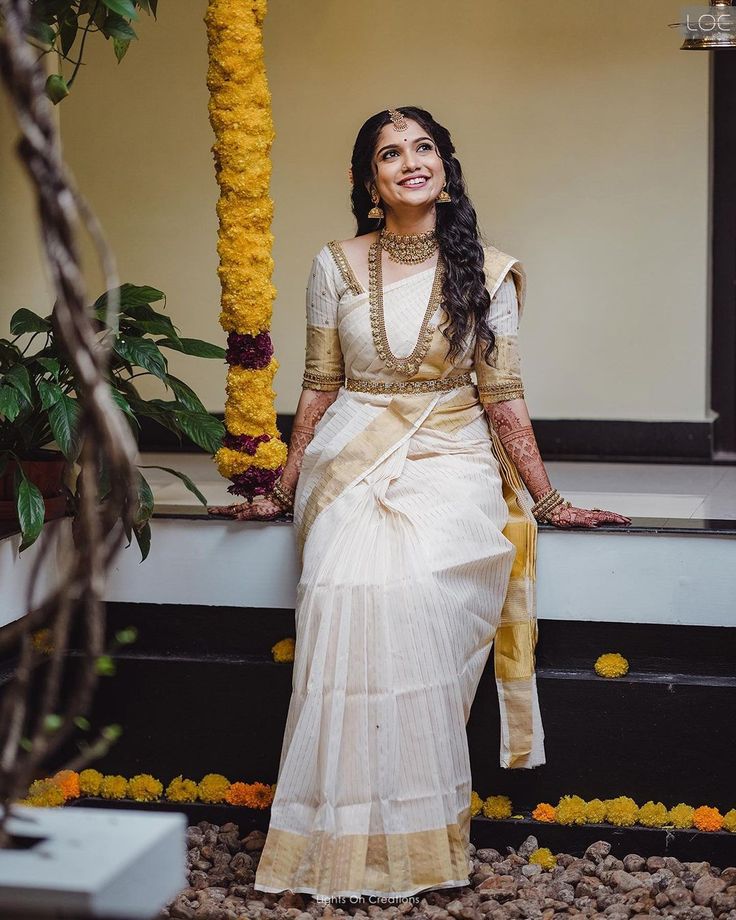 a woman in a white and gold sari sitting on a ledge next to flowers