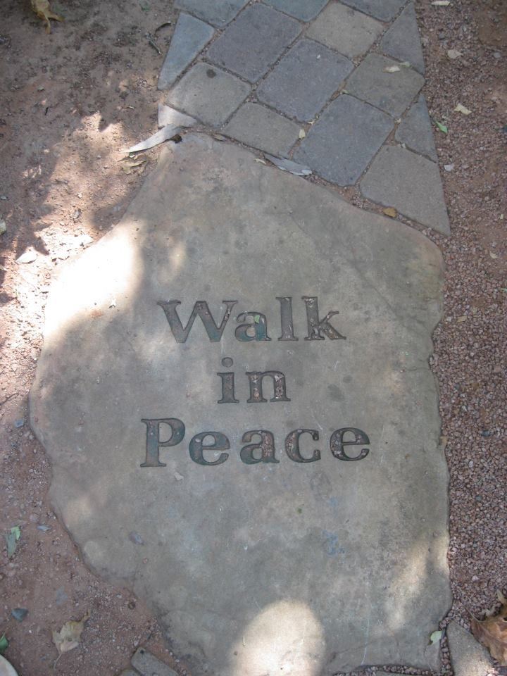 a stone with the words walk in peace written on it next to a brick walkway