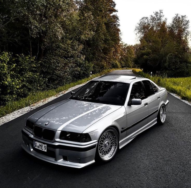 the silver car is parked on the side of the road in front of some trees