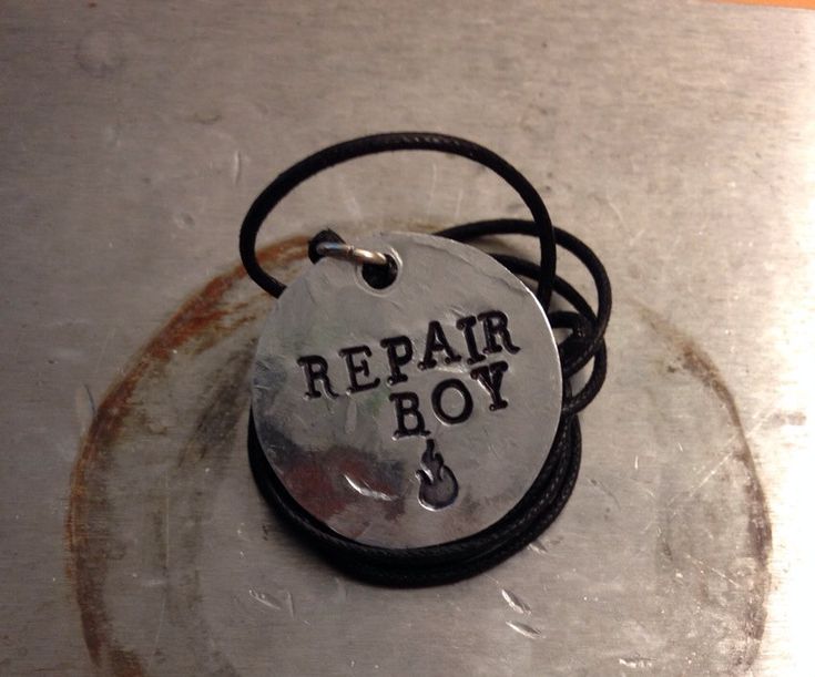 a necklace with the words repair boy on it sitting on top of a piece of metal