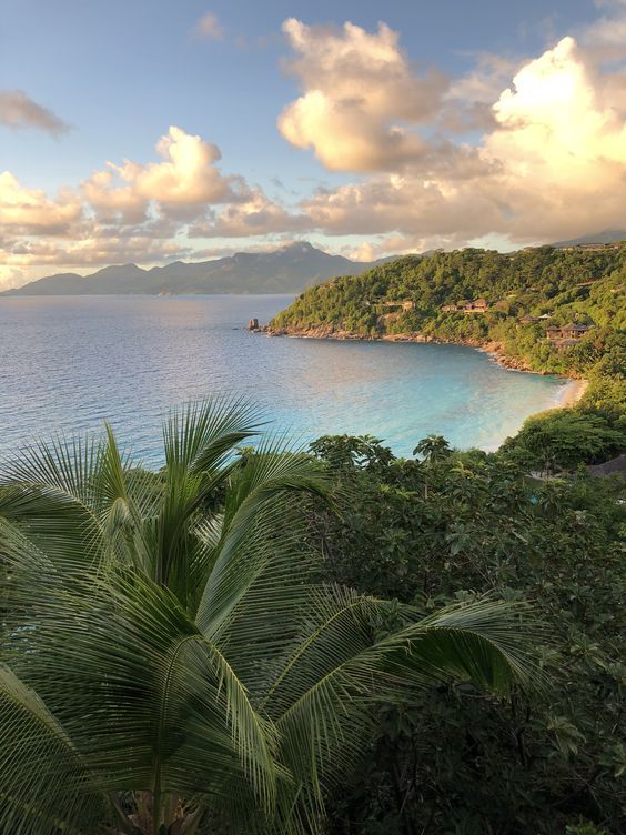 the ocean is surrounded by lush green trees and blue skies with clouds in the background