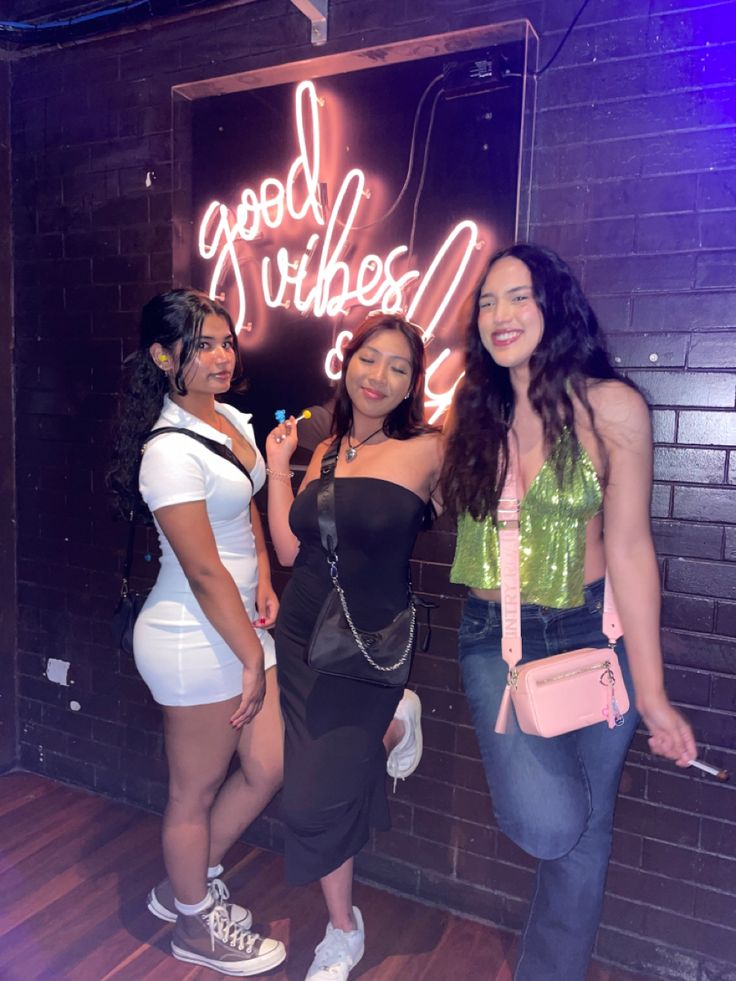 three women standing next to each other in front of a neon sign