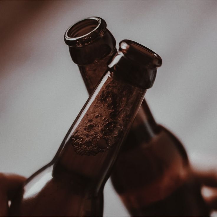 two brown beer bottles being held by someone's hands