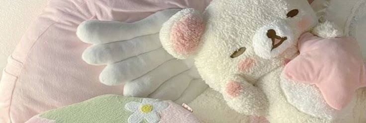 a white teddy bear laying on top of a pink pillow next to other stuffed animals