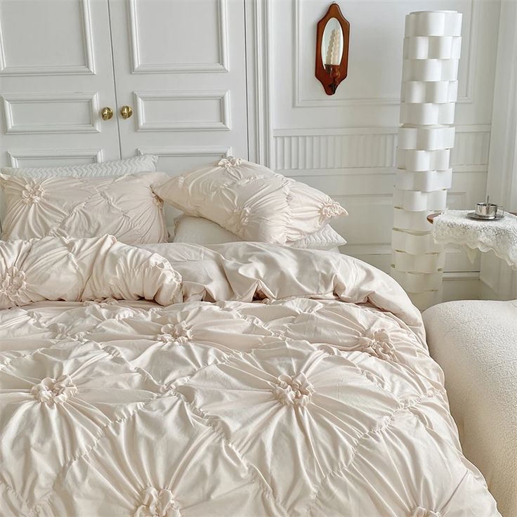 a bed with white comforters and pillows in a room next to a mirror on the wall