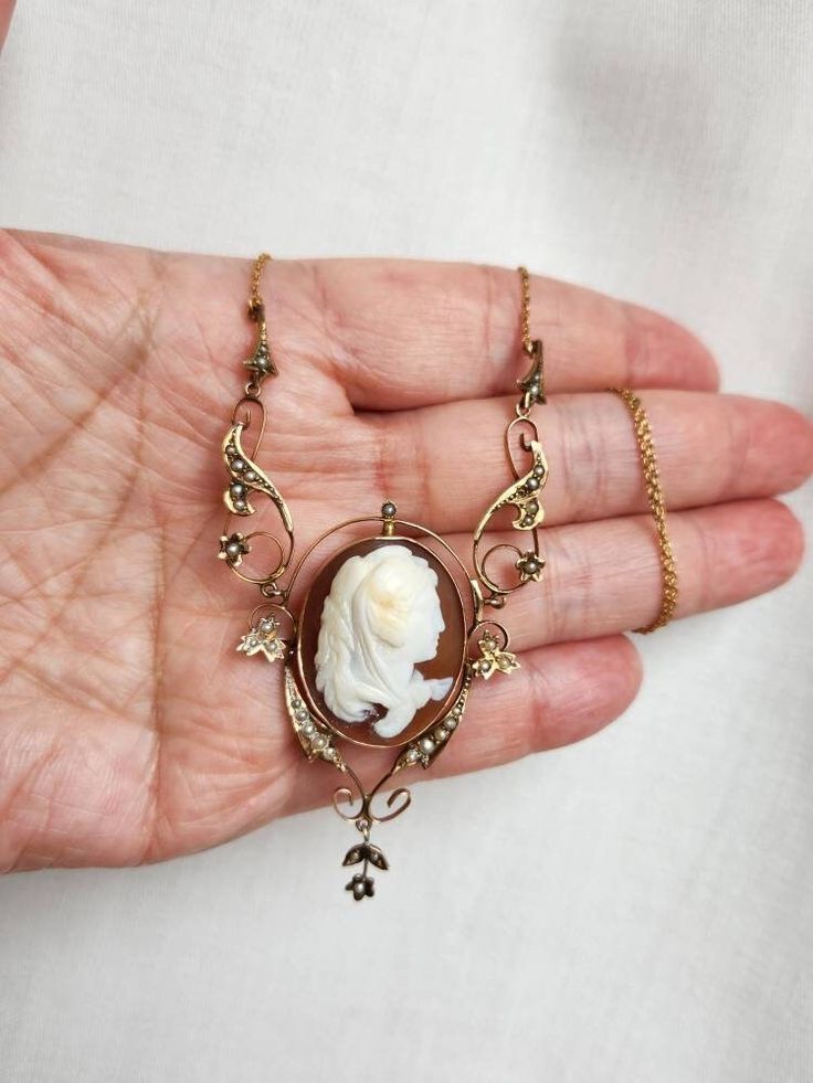 An absolutely stunning antique lavalier modelled in 9k yellow gold. The focal point of this piece is the large cameo centre made of carved shell. The ornate leaves are adorned with creamy seed pearls.  This lavalier is on the shorter side, measuring approximately 16 inches  (40.5cm) in length. The cameo (excluding the decorative seed pearls) is 2.5x2cm. The drop pendant measures an impressive 5cm from top to bottom. Gross weight is 8.92g.  This beautiful lavalier is so pretty and eye catching. I Collectible Art Nouveau Carved Jewelry, Victorian Cabochon Necklace For Wedding, Antique Carved Yellow Gold Necklaces, Antique Cabochon Necklaces For Wedding, Vintage Yellow Gold Intaglio Necklace, Antique Gold Necklace With Carved Details, Heirloom Style Cameo Medallion Necklace, Heirloom Cameo Medallion Necklace, Gold Carved Victorian Necklace