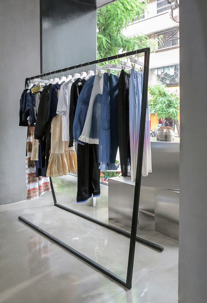 clothes are hanging on racks in front of a large mirror that is reflecting the building's windows