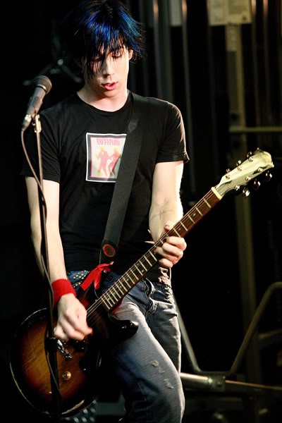 a young man with blue hair playing an electric guitar in front of a microphone on stage