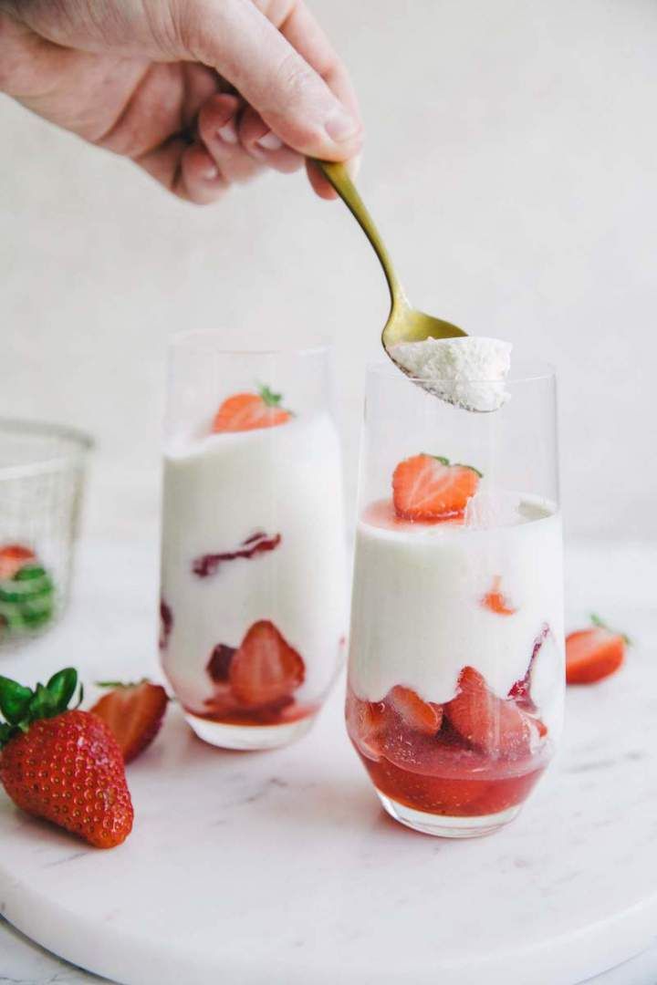 someone is spooning strawberries into two glasses with yogurt and strawberry sauce