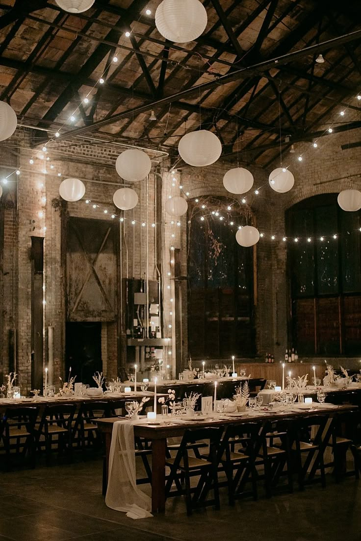 a long table is set up with white paper lanterns hanging from the ceiling and candles on the tables