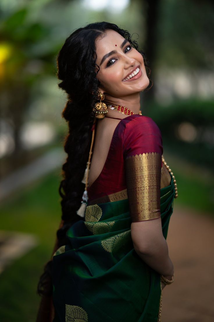 a woman with long hair wearing a green and red sari smiling at the camera