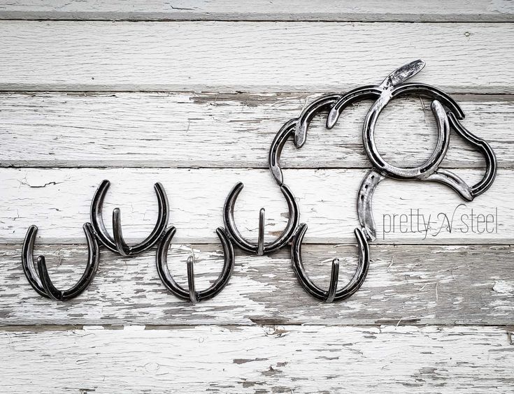 four metal hooks are hanging on the side of a white wood planked wall, with one hook in the shape of a horse's head