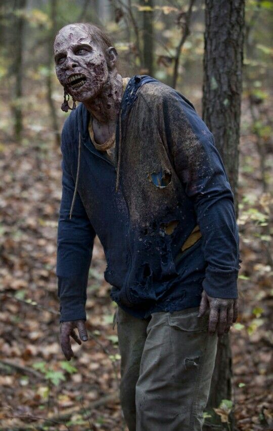 a man in the woods with his face covered in mud and blood, walking through leaves