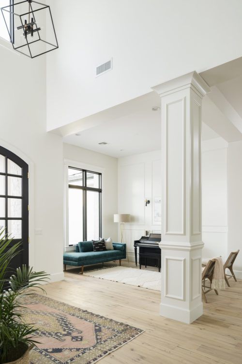 a living room filled with furniture next to a tall white columned wall and windows