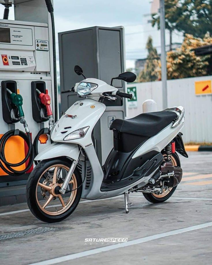 a motor scooter parked in front of a gas station with an open fuel pump