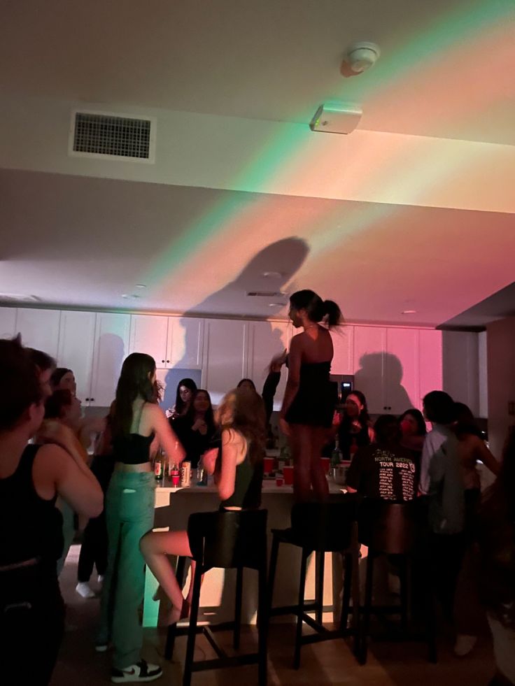 a group of people standing around in a room with pink and green lights on the ceiling