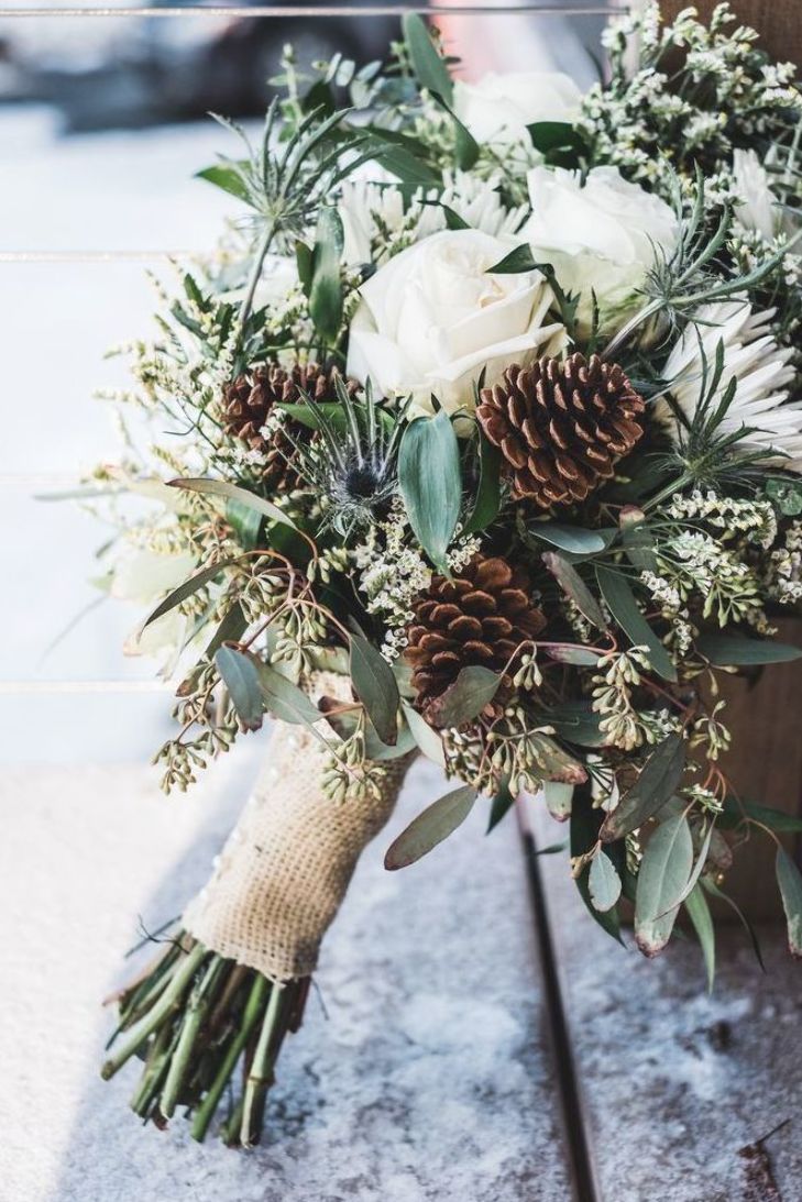 a bridal bouquet with pine cones and greenery is sitting on a wooden bench