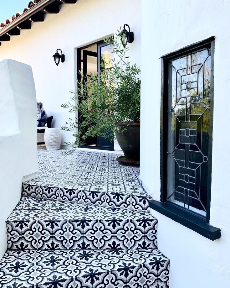 a black and white tiled walkway leading up to a house with potted plants on it