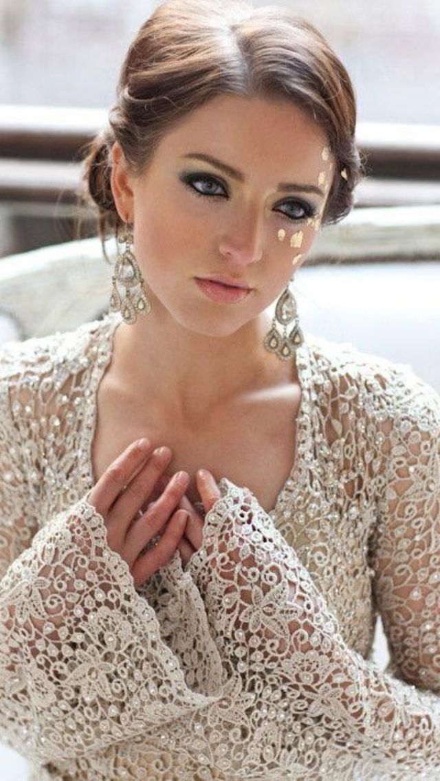 a woman in a white lace dress with her hands on her chest and wearing earrings