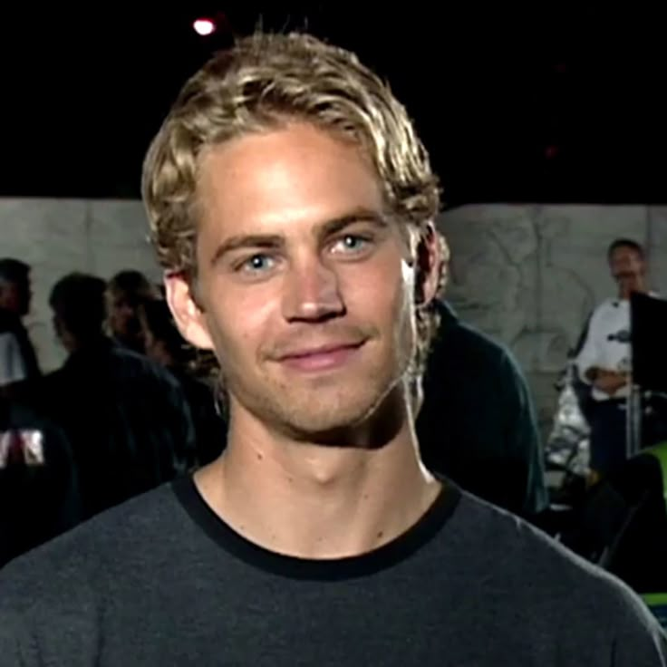 a man with blonde hair and blue eyes standing in front of a group of people