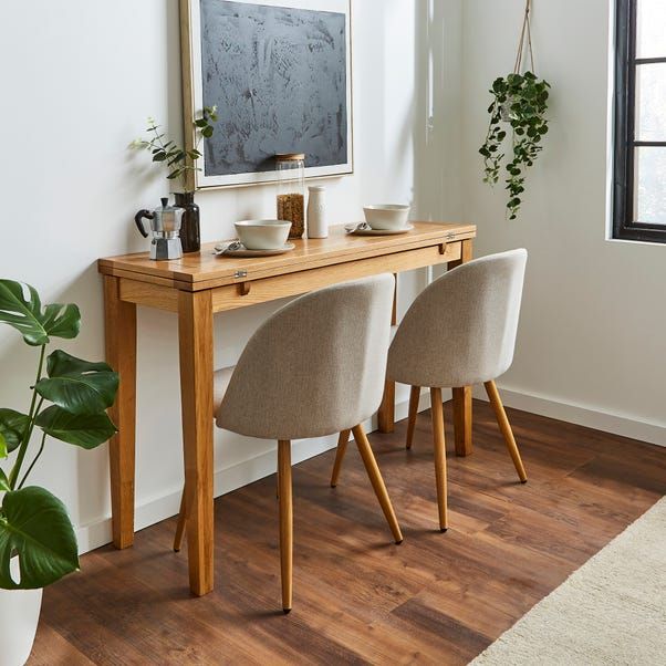 two chairs sitting at a wooden table in front of a window with potted plants