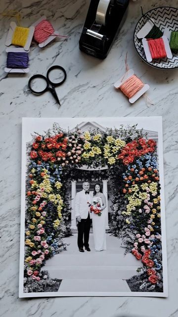 a couple standing in front of a floral arch with scissors and thread on the table