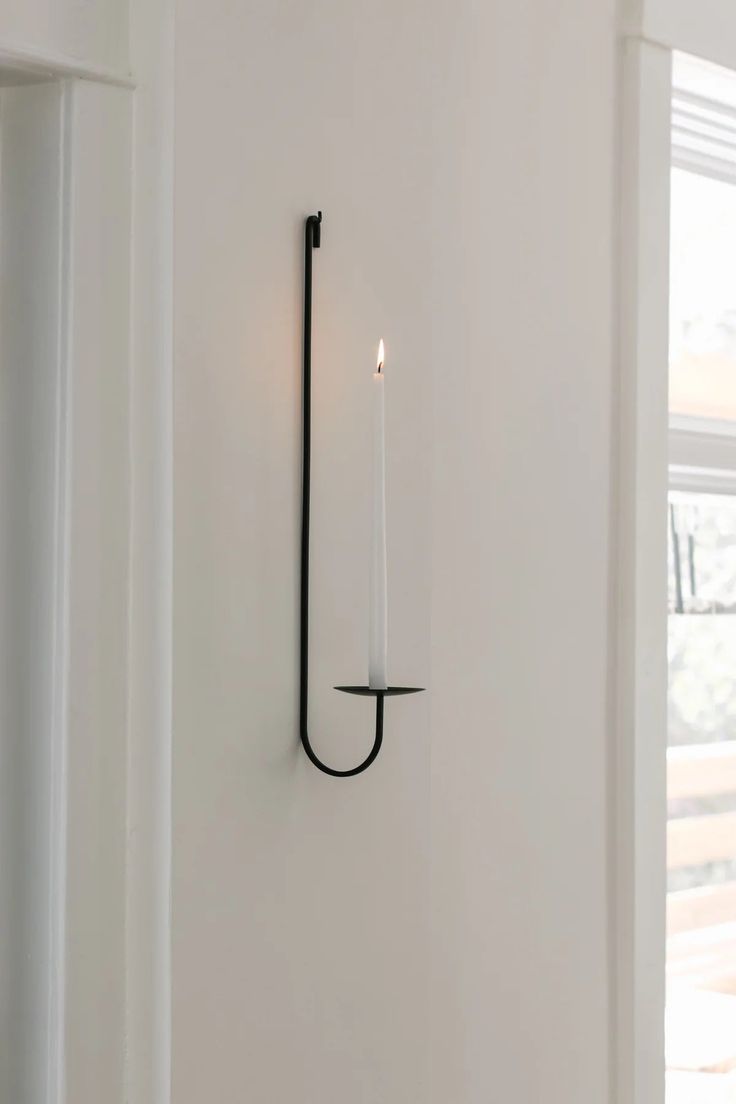 a candle is lit on the wall next to an open window in a white room