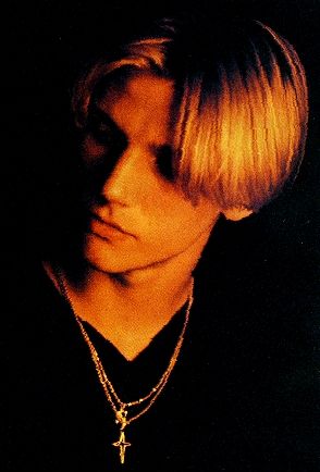 a young man with blonde hair wearing a necklace and black shirt is staring at the camera