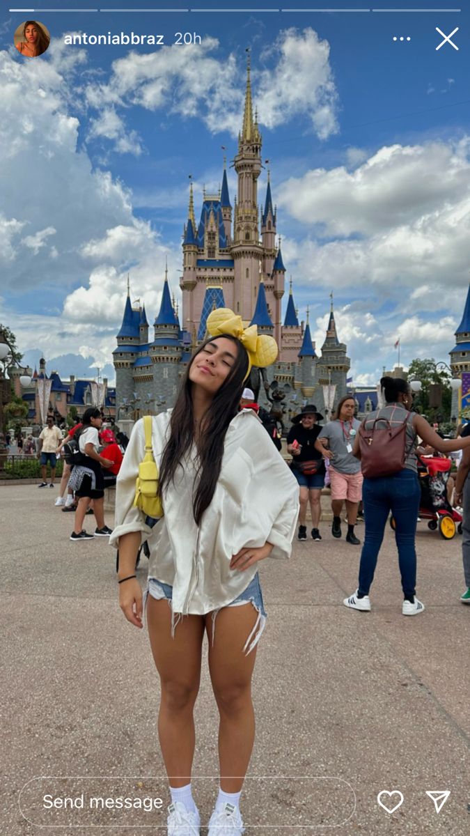 a woman standing in front of a castle wearing shorts and a yellow hat with her hands on her hips