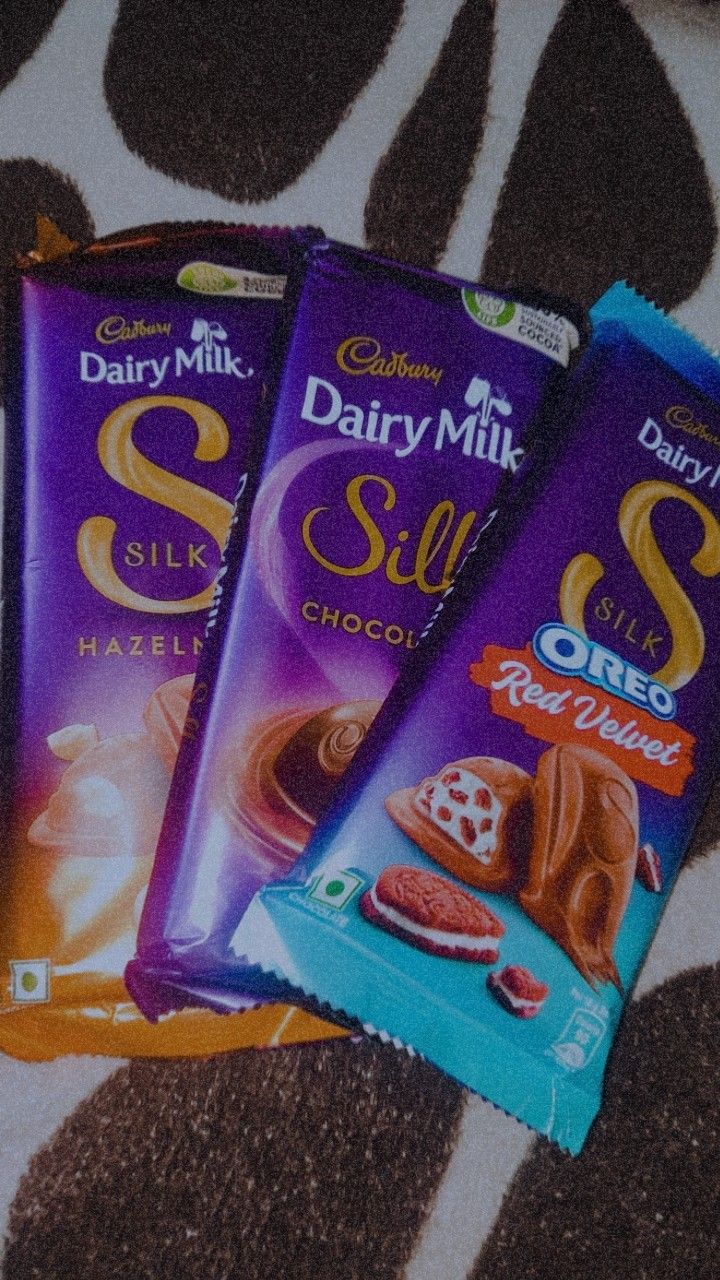 three dairy milk chocolate bars sitting on top of a bed next to eachother